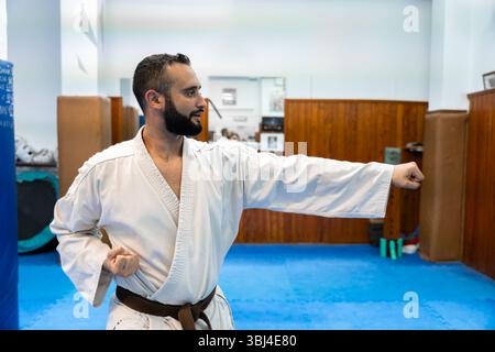 Praticien de karaté exécutant une technique de poinçon précise, mettant en valeur la puissance et le contrôle pendant la pratique dans un environnement de dojo traditionnel Banque D'Images