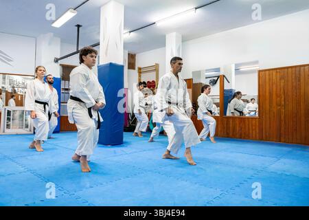 Groupe de karatéka portant du GI blanc pratiquant le kata sur tapis bleu dans le dojo avec instructeur Banque D'Images