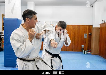Deux maîtres de karaté pratiquant les techniques de combat dans un dojo Banque D'Images
