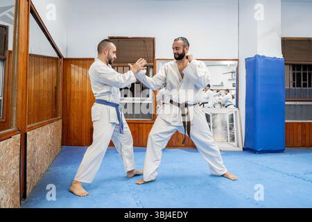 Deux hommes pratiquant le karaté dans un dojo, portant des kimonos blancs et des ceintures, effectuant un mouvement défensif Banque D'Images