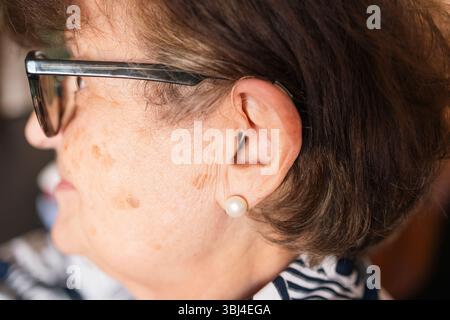 Profil rapproché d'une femme âgée portant une prothèse auditive et des lunettes, mettant en évidence la technologie d'assistance pour la perte auditive Banque D'Images