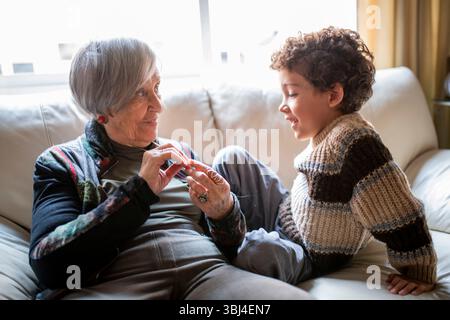 Grand-mère et petit-enfant sont assis sur un canapé, jouant un jeu de doigts et souriant l'un à l'autre Banque D'Images
