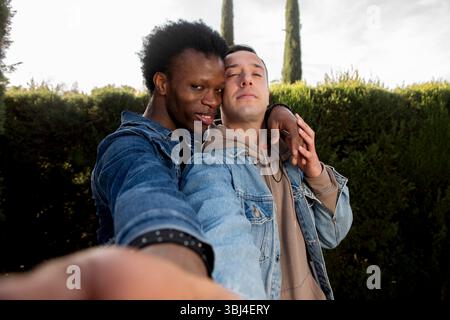 Deux hommes embrassant et prenant un selfie dans un parc, célébrant leur amour et leur relation Banque D'Images