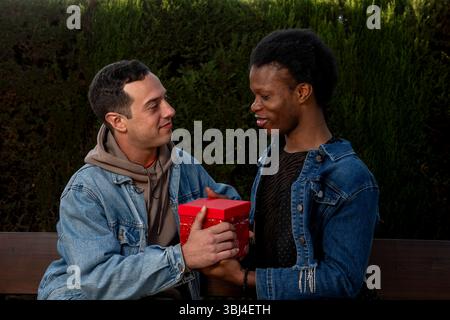 Amoureux petits amis échangeant des cadeaux assis sur un banc dans un parc Banque D'Images