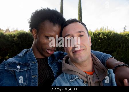 Couple gay interracial embrassant dans un parc, prenant un selfie Banque D'Images