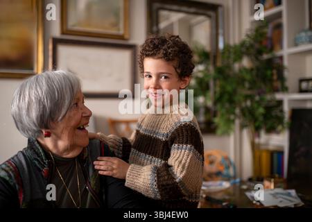 Heureux petit-fils embrassant sa grand-mère à la maison, à la fois souriant et partageant un moment d’amour et de complicité Banque D'Images