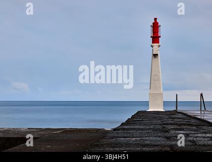 Le petit phare d'entrée du port rouge de Caloura sur l'île de São Miguel dans les Açores du Portugal. Banque D'Images