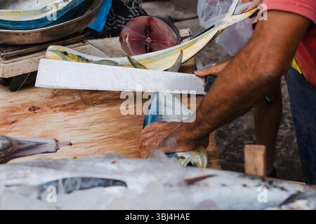 Un vendeur masculin dans un marché aux poissons coupe du poisson avec un couteau, Sicile Banque D'Images