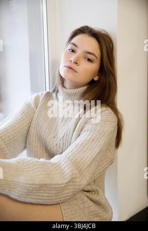 Jeune femme en pull assise sur le rebord de la fenêtre Banque D'Images