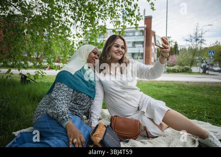 Deux femmes ethniquement diverses prenant un selfie sur une couverture de pique-nique Banque D'Images
