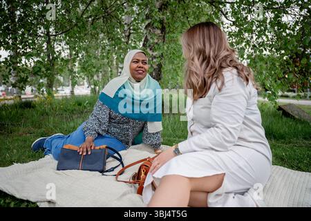 Deux femmes de différentes ethnies parlant sur une couverture de pique-nique dans le parc Banque D'Images