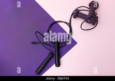 Corde à sauter et haltères sur tapis de yoga violet avec fond rose Banque D'Images