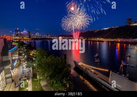 Des feux d'artifice colorés explosent au-dessus du point State Park à Pittsburgh la nuit, avec des bateaux visibles sur la rivière Ohio lors d'une célébration du 4 juillet. Banque D'Images