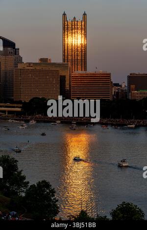La lumière dorée du soleil se reflète sur le verre du bâtiment PPG à Pittsburgh dans un cadre vertical, avec des bateaux visibles sur la rivière Ohio au premier plan. Banque D'Images