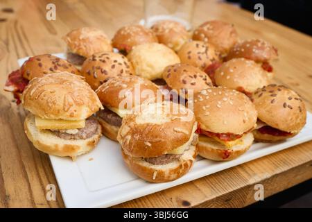 Délicieux mini hamburgers garni de fromage, bacon et plus encore, magnifiquement disposés sur un plateau blanc, parfaits pour servir à n'importe quel rassemblement Banque D'Images