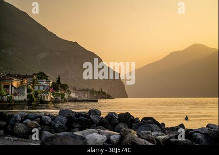 Lever de soleil coloré sur le lac de Garde en Italie, avec l'eau du lac calme au premier plan et les montagnes brumeuses en arrière-plan créant un calme, serein. Banque D'Images