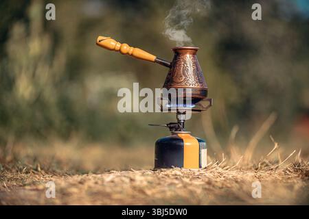 Infusion du café dans le cezve turc sur brûleur à gaz pour le camping. Feu avec flamme bleue et vapeur sur un délicieux café chaud dans la nature sauvage Banque D'Images