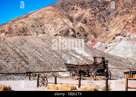 Un chariot en bois antique, une relique du passé, se dresse au premier plan sur un fond de montagne accidenté. Il sert de rappel aux pionniers Banque D'Images