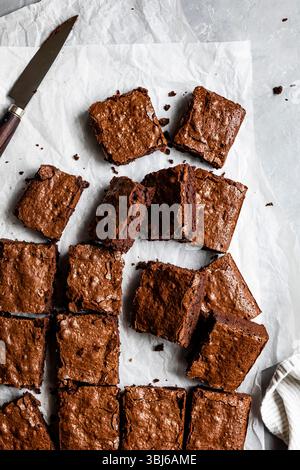 Une vue aérienne de brownies au chocolat coupés en carrés sur du papier parchemin, avec un couteau à proximité. Banque D'Images