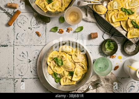 Raviolis cuits dans différentes casseroles avec des verres à vin et du liège, des feuilles de basilic et des noix, de l'huile d'olive sur le dessus de table carrelé, nourriture typique de Ligurie, Italie Banque D'Images
