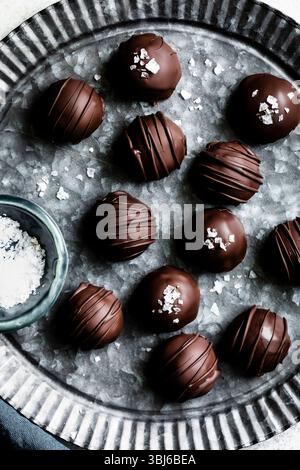 Un assortiment de truffes au chocolat au sel de mer sur un plateau métallique texturé. Banque D'Images