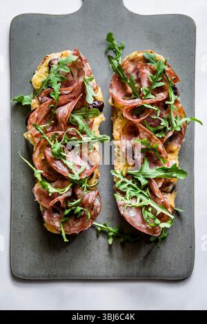 Deux sandwichs ouverts avec salami et roquette sur une planche à découper. Banque D'Images