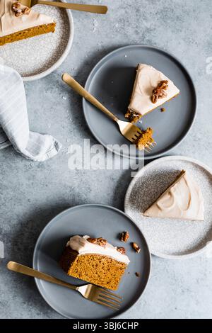 Trois tranches de gâteau givré avec des pacanes sur des assiettes, accompagnées de fourchettes dorées sur une surface texturée. Banque D'Images