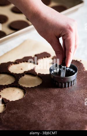 Une personne utilise un emporte-pièce rond pour couper des formes de pâte au chocolat sur du papier parchemin. Banque D'Images