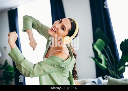Femme adorable appréciant la musique avec des écouteurs à l'intérieur, exprimant la joie et le bonheur dans un environnement élégant et relaxant à la maison Banque D'Images