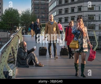 LES TRAVAILLEURS DE LA VILLE MENDIANT LA TASSE MENDIANTE VILLE Canary Wharf les travailleurs de Londres intelligemment habillés dans le quartier des bureaux financiers publics, marchant devant un homme âgé assis éclairé par le coucher du soleil, appelant de l'argent comptant avec sa tasse en plastique prolongée LONDRES Royaume-Uni Banque D'Images