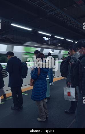 Attendant silencieusement la ligne Yamanote, les têtes se sont inclinées au-dessus de leurs téléphones tandis que le train passe dans un flou de mouvement Banque D'Images
