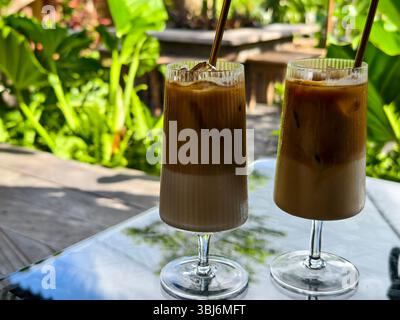 Deux lattes glacés servis dans de grands gobelets en verre avec des pailles écologiques dans un café de jardin tropical Banque D'Images
