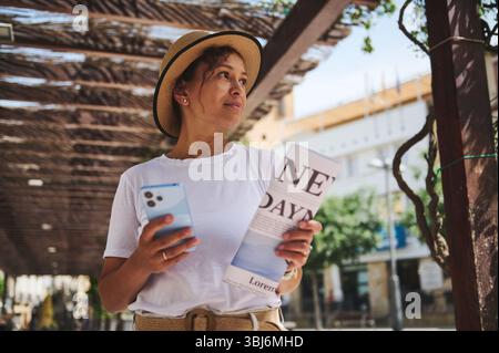 Une femme explore un quartier historique marchant sous des pergolas tenant un smartphone et un guide. Elle aime le voyage touristique dans un e charmant et ensoleillé Banque D'Images