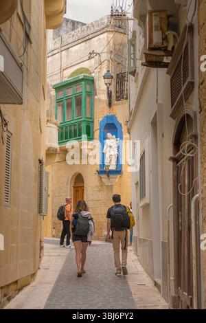 Voyage jeune couple, vue arrière de touristes portant des sacs à dos explorant un quartier dans le quartier pittoresque de la vieille ville de Victoria (Rabat), Gozo, Malte Banque D'Images