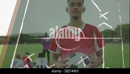 Debout sur un terrain en herbe, joueur portant un maillot rouge et tenant un ballon de soccer, avec entraîneur, coéquipiers Banque D'Images