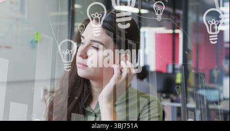 Regarder femme portant une chemise verte se brossant les cheveux au bureau avec des superpositions de moniteur et des panneaux rouges Banque D'Images