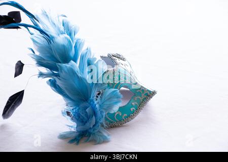 Masque de carnaval bleu clair avec des plumes bleu clair et noir sur un fond rose clair, accessoire décoratif pour une mascarade Banque D'Images