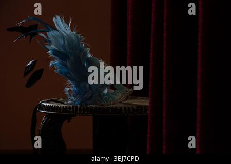 Masque de carnaval repose sur une chaise près d'un miroir et un rideau rouge dans une pièce dans l'obscurité, masque de théâtre Banque D'Images