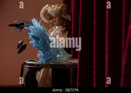 Masque de carnaval repose sur une chaise et un rideau rouge et derrière il y a une poupée dans la chambre, masque de théâtre Banque D'Images