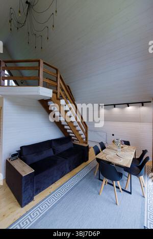 Une vue intérieure magnifique mettant en valeur un salon moderne avec un canapé sombre, escalier en bois et salle à manger, créant une atmosphère chaleureuse et accueillante Banque D'Images