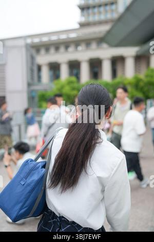 Au début de l'été à Shanghai, près du Bund, des lycéennes japonaises en uniforme marchent à travers une foule, vues de derrière, leur présence ajoutant de la jeunesse Banque D'Images