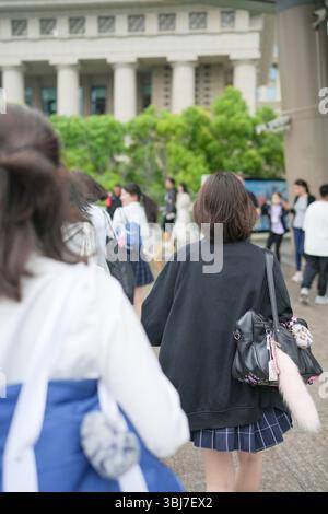 Au début de l'été à Shanghai, près du Bund, des lycéennes japonaises en uniforme marchent à travers une foule, vues de derrière, leur présence ajoutant de la jeunesse Banque D'Images