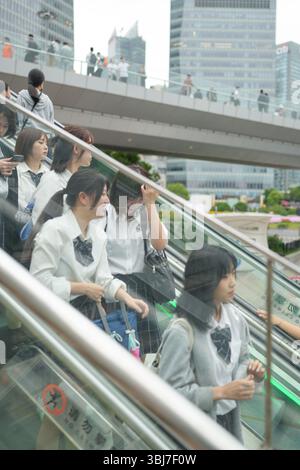 Au début de l'été à Shanghai, près du Bund, des lycéennes japonaises en uniforme descendent un escalator avec des gratte-ciel derrière elles, leur assortiment o Banque D'Images