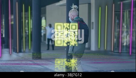 Homme marchant portant un masque et un sweat à capuche olive tenant un smartphone sur une passerelle couverte, affichant un code QR Banque D'Images