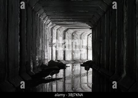 Un tunnel de drainage carré en béton avec une lumière à l'extrémité qui brille du tournant du tunnel. Banque D'Images