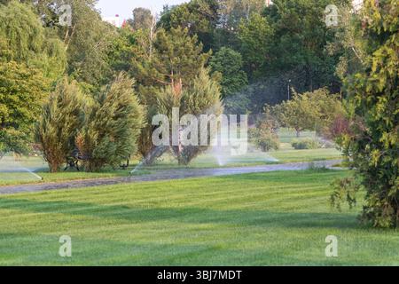 Une gamme de gicleurs pulvérisant de l'eau à travers l'herbe verte, entouré d'arbres et de buissons sur un vaste terrain de golf en été. Banque D'Images