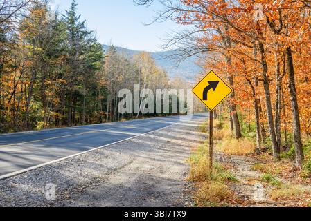 Panneau de signalisation jaune avertissant les conducteurs d'un virage dangereux le long d'une route de montagne par un jour clair d'automne Banque D'Images