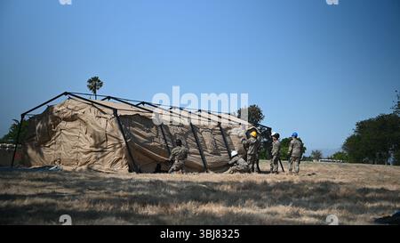 Des aviateurs du 23e escadron de communications de combat sécurisent des couvertures sur une tente de communication pour étendre les services de routeur de protocole Internet non sécurisé (NIPR) pour une base aérienne expéditionnaire (XAB) lors d'un déploiement simulé pour l'exercice NEXUS RISING 25-01 à la base aérienne de Travis, Calif, le 5 juin 2025. Les Airmen, certains agenouillés pour ajuster les sangles, ont travaillé à préparer le XAB situé dans un emplacement simulé du United States Indo-Pacific Command. NEXUS RISING 25-01 est un exercice de préparation à grande échelle conçu pour améliorer la capacité de générer et de maintenir la mobilité des aviateurs prêts au combat et de se déployer rapidement en tant que Banque D'Images