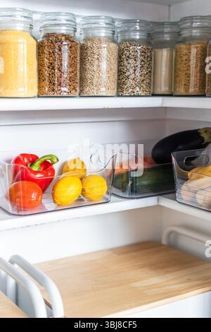 petit garde-manger organisé avec des bocaux transparents assortis remplis de céréales, légumineuses, épices et produits frais dans des récipients, alimentation saine, maison rangée, organi Banque D'Images