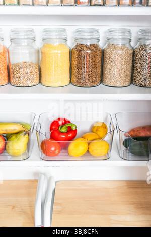 petit garde-manger organisé avec des bocaux transparents assortis remplis de céréales, légumineuses, épices et produits frais dans des récipients, alimentation saine, maison rangée, organi Banque D'Images